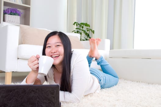 Portrait of attractive Asian girl using laptop and drinking coffe. Young woman indoors living lifestyle at home.