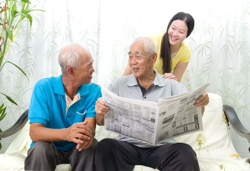 Portrait of chinese family reading newspaper together at home. Mature 70s senior man and his children.