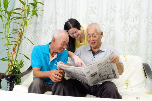 Portrait of chinese family reading newspaper together at home. Mature 70s senior man and his children.