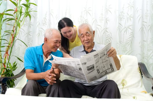 Portrait of chinese family reading newspaper together at home. Mature 70s senior man and his children.