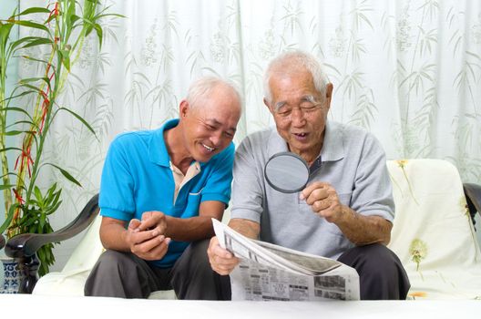 Portrait of chinese family reading newspaper together at home. Mature 80s senior man and his son