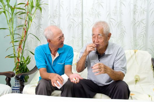 Asian senior man having medicine at home. Adult son caring for a senior man.
