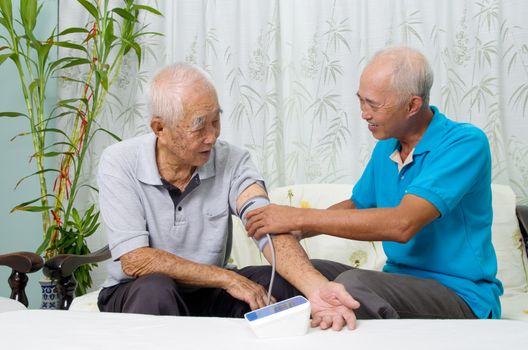Asian man is checking taking his father's blood pressure.