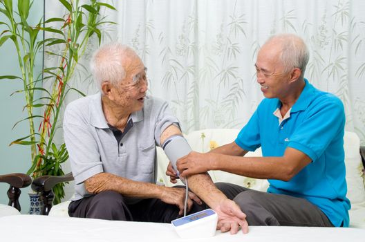Asian man is checking his father's blood pressure.