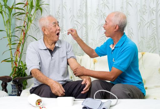 Asian man is checking his father's body temperature with a digital thermometer.