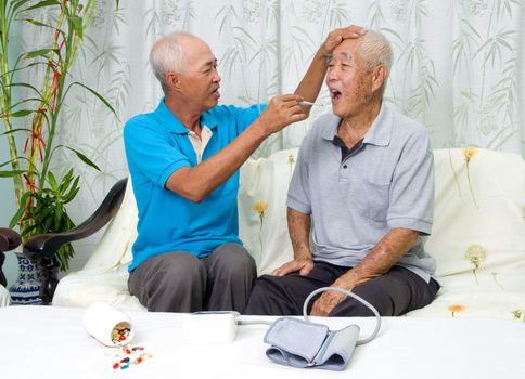 Asian man is checking his father's body temperature with a digital thermometer.