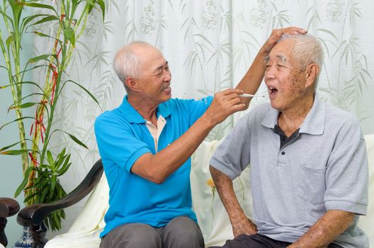 Asian man is checking his father's body temperature with a digital thermometer.