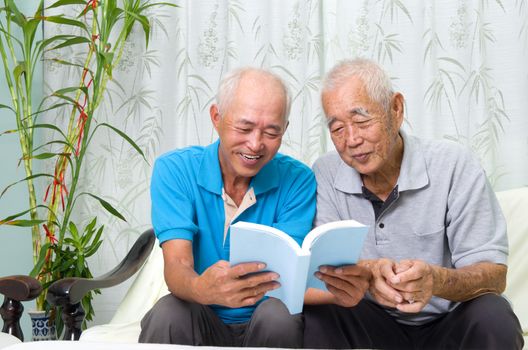 asian senior man reading a book with his son at home