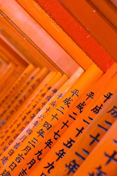 Red wooden Tori Gate at Fushimi Inari Shrine in Kyoto, Japan. Selective focus on traditional japanese writing.