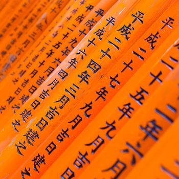 Red wooden Tori Gate at Fushimi Inari Shrine in Kyoto, Japan. Selective focus on traditional japanese writing.