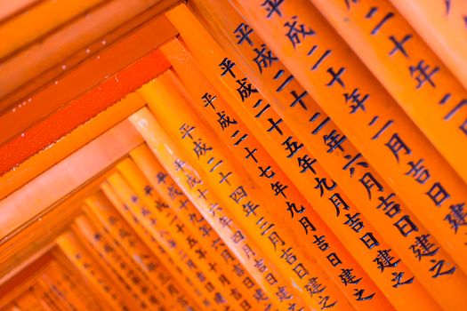 Red wooden Tori Gate at Fushimi Inari Shrine in Kyoto, Japan. Selective focus on traditional japanese writing.