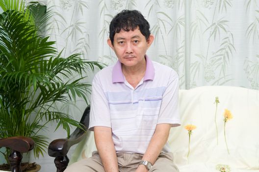 Mentally disabled man sitting on the sofa at home looking at camera.