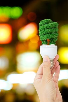 hand holding green light bulb and defocused city night light background, eco energy concept