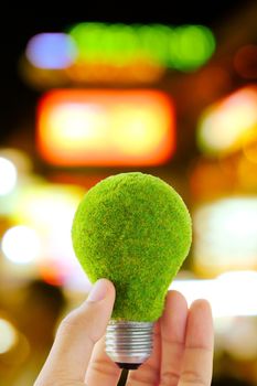 hand holding green light bulb and defocused city night light background, eco energy concept