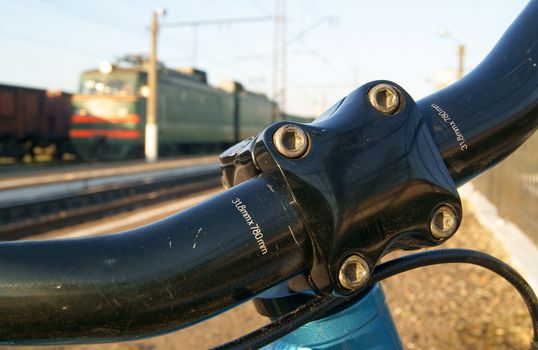 Closeup of bicycle handlebar and a train coming backstage at railway station