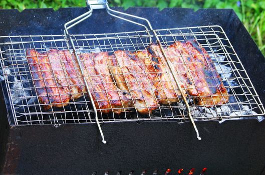 Grilled pork ribs on metal grid over open fire, barbecue