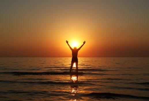 Silhouette of a male with raised arms in the sea water at sunset