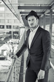 Head and Shoulders Portrait of Stylist Young Man Wearing Suit and Hat Looking at Camera While Standing on Moving Sidewalk in Building