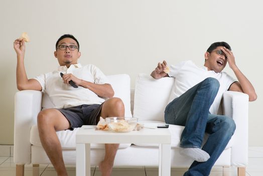 Group of men sitting on sofa watching live sport together at home.