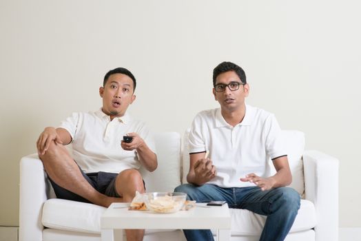Group of men sitting on sofa watching sport together at home.