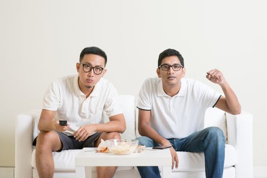 Men sitting on couch watching football match on television, Asian people friendship at home.