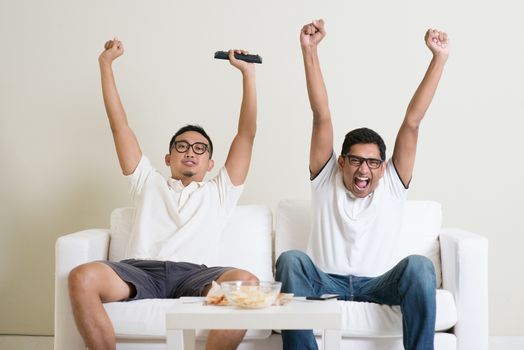 Friendship, technology and home concept. Happy male friends with remote control and junk food at home.