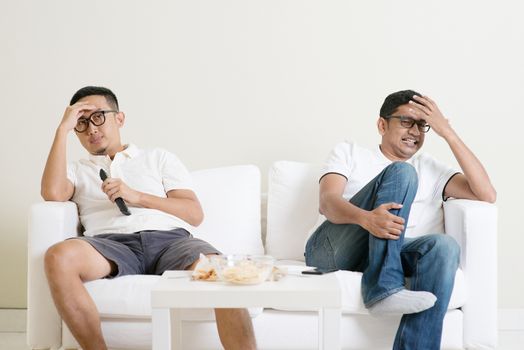 Men sitting on couch watching football match on television together at home.