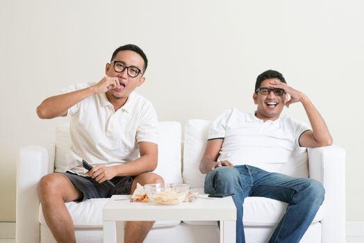 Friendship, technology and home concept. Male friends with remote control and junk food at home.