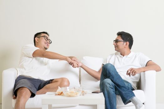 Man sitting on sofa and handshaking with friend at home. Multiracial people friendship.