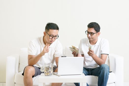 Young guys counting cash with partner, earning money from their successful online business. Asian men working from home.