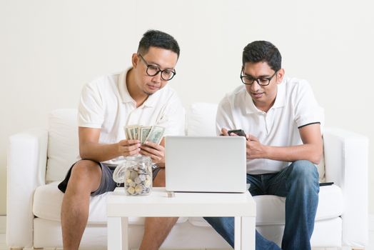 Business website concept. Young guys counting cash with partner, earning money from their successful online business. Asian men working from home.