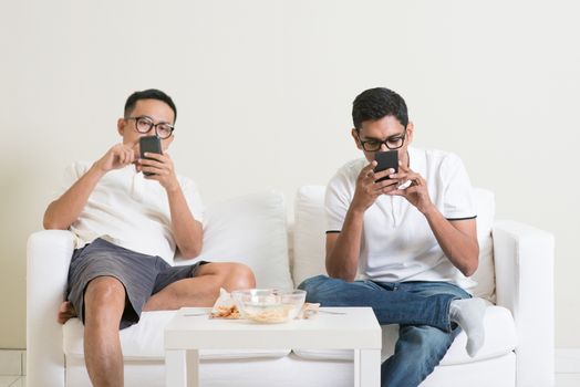 Friends sitting on sofa and playing on their phones at home.