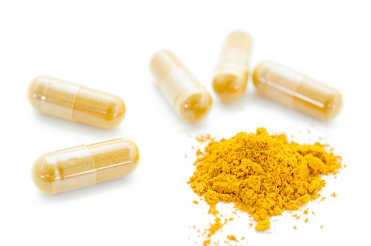 Turmeric powder and herbal capsules on white background.