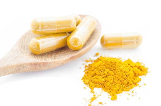 Turmeric powder and a wooden spoon with herbal capsule on white background.