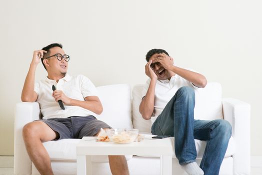 Men sitting on couch watching movie on television together at home.