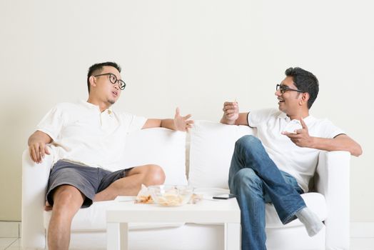 Men talk concept. Two young male friend sitting on sofa and chatting at home. Multiracial people friendship.