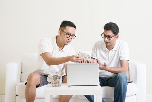 Internet marketing concept. Young guys counting cash with partner, earning money from their successful online business. Asian men working from home.