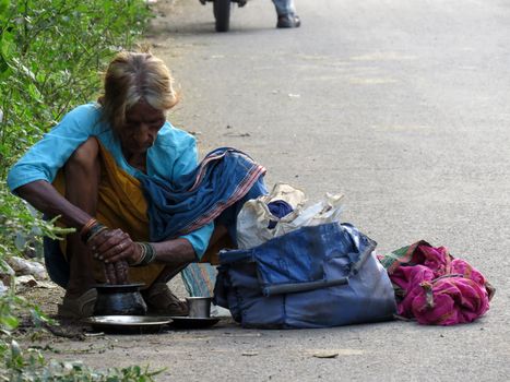 An elderly homeless woman from India washing her hands in the utensils after her meal.                               