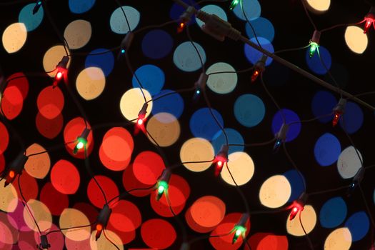 An abstract background of a festive lights wire mesh against the backdrop of colorful blur lights.