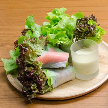 Salad roll vegetables and crab stick with salad dressing in wooden plate