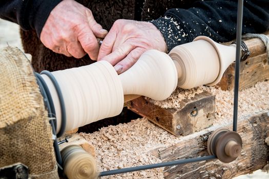 An artisan carves a piece of wood using an old manual lathe.