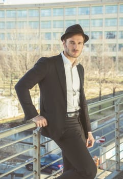 Head and Shoulders Portrait of Stylist Young Man Wearing Suit and Hat Looking at Camera While Standing on Moving Sidewalk in Building