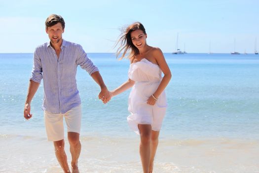 Cheerful couple walking on beach on blue sea background