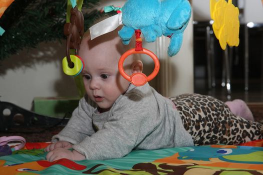 Happy baby girl playing on the floor surrounded surrounded by toys