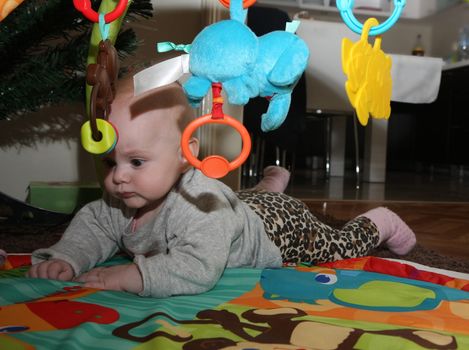 Happy baby girl playing on the floor surrounded surrounded by toys