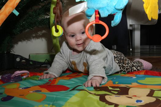 Happy baby girl playing on the floor surrounded surrounded by toys