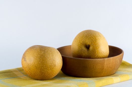Asian pears, rustic wooden bowl, and yellow plaid napkin on white background