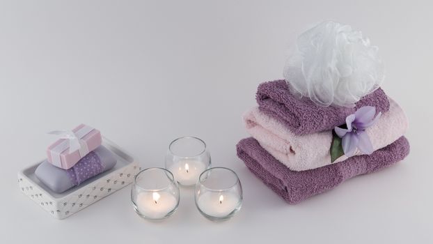 Fancy bath soap and towels with lit candles on white background