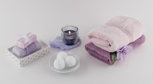 Fancy bath soap, bath bombs, spa towels, and lit aromatherapy candle on white background