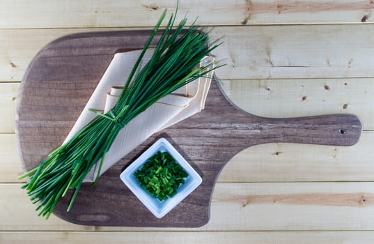 Fresh chives on pale yellow napkin and wooden board